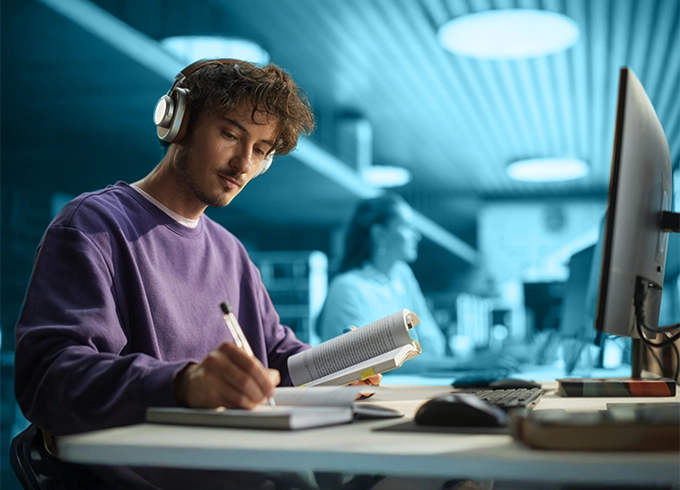 Feature tile which is a photo of a student studying in the library in the evening